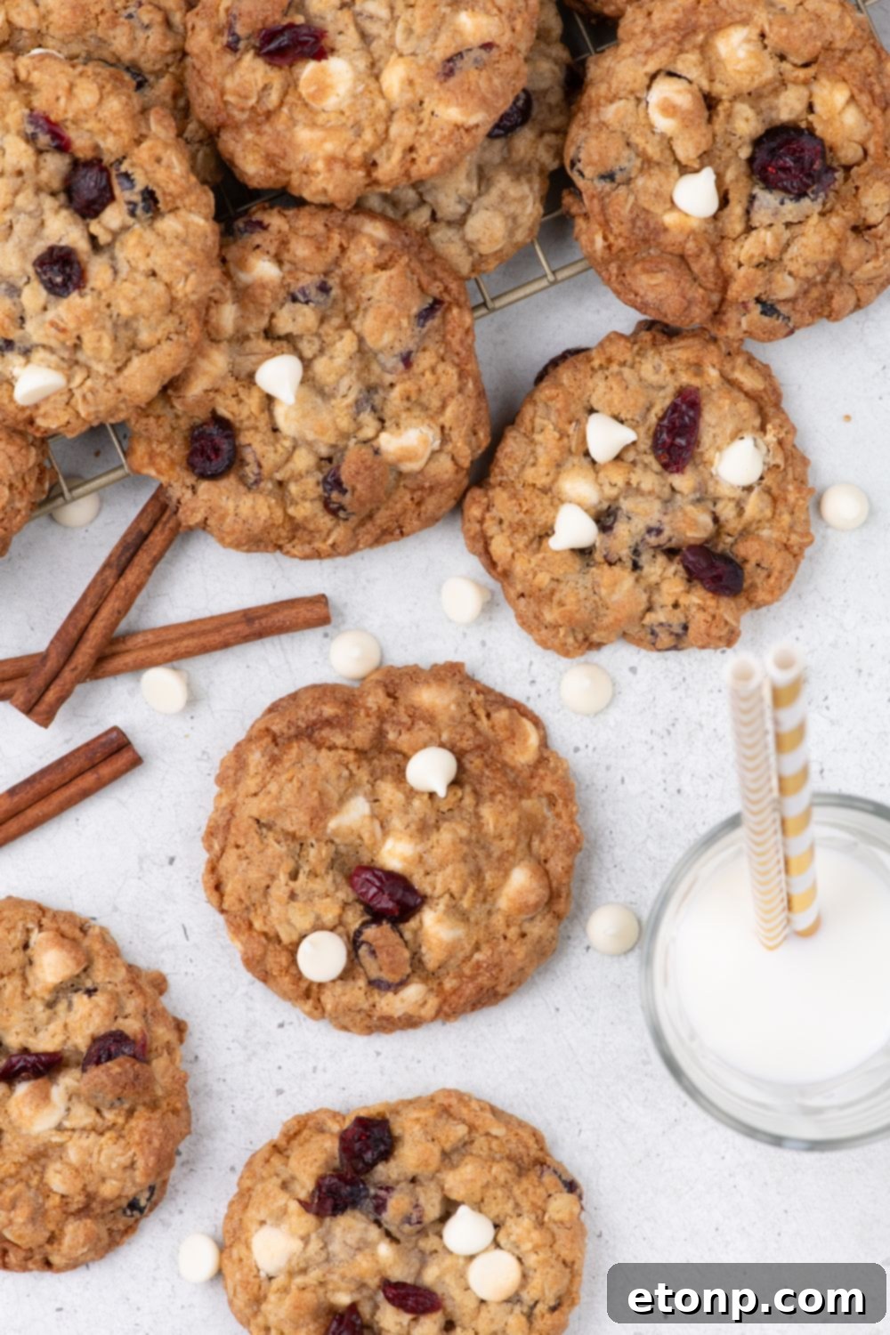 White Chocolate Cranberry Oatmeal Cookies spread out on table with a glass of milk with straws in it 