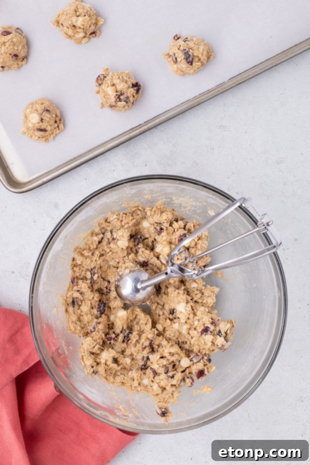 bowl of raw White Chocolate Cranberry Oatmeal Cookie dough on table with baking sheet behind it 
