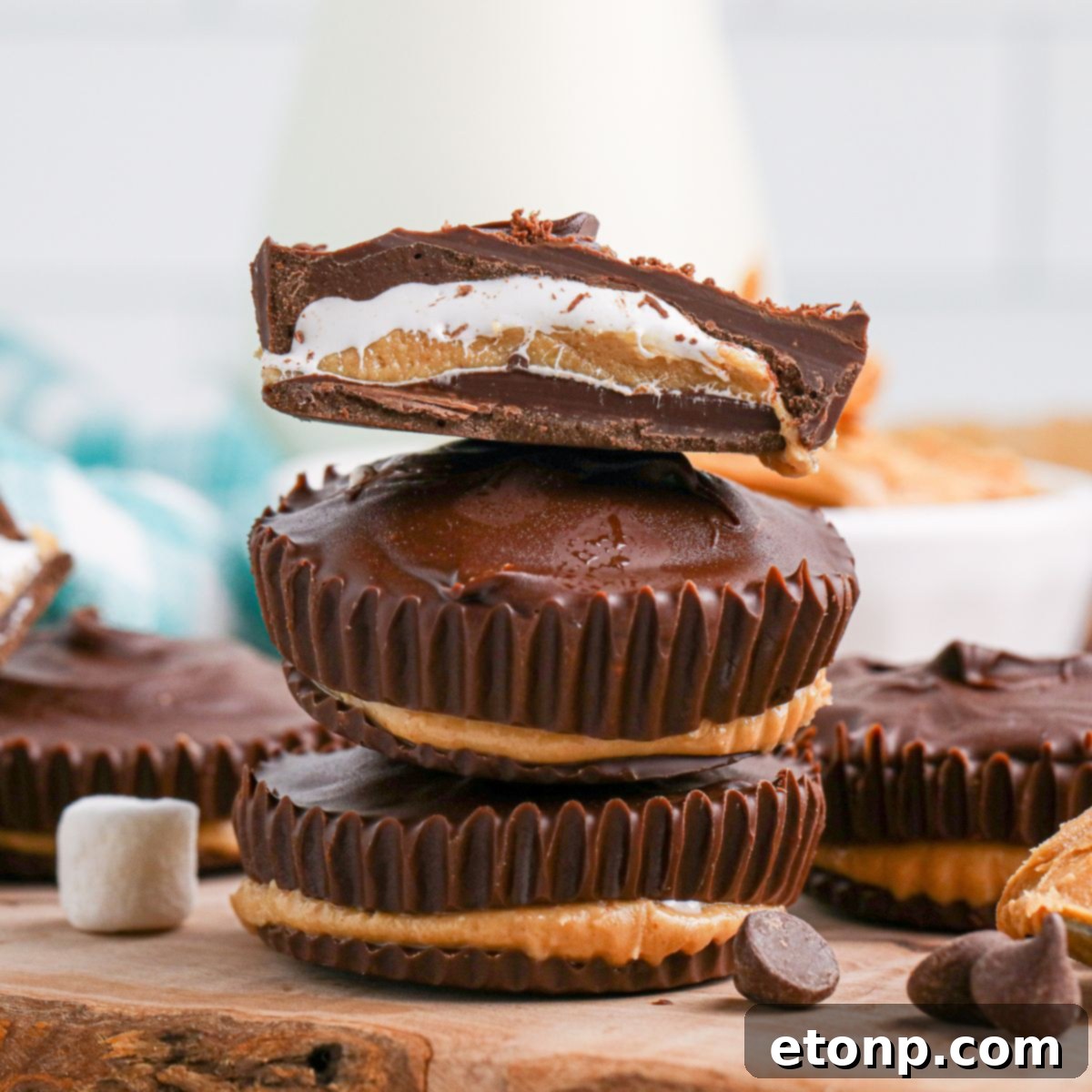 Peanut Butter Marshmallow Cups stacked on wooden cutting board with top one cut in half so you can see the layers 