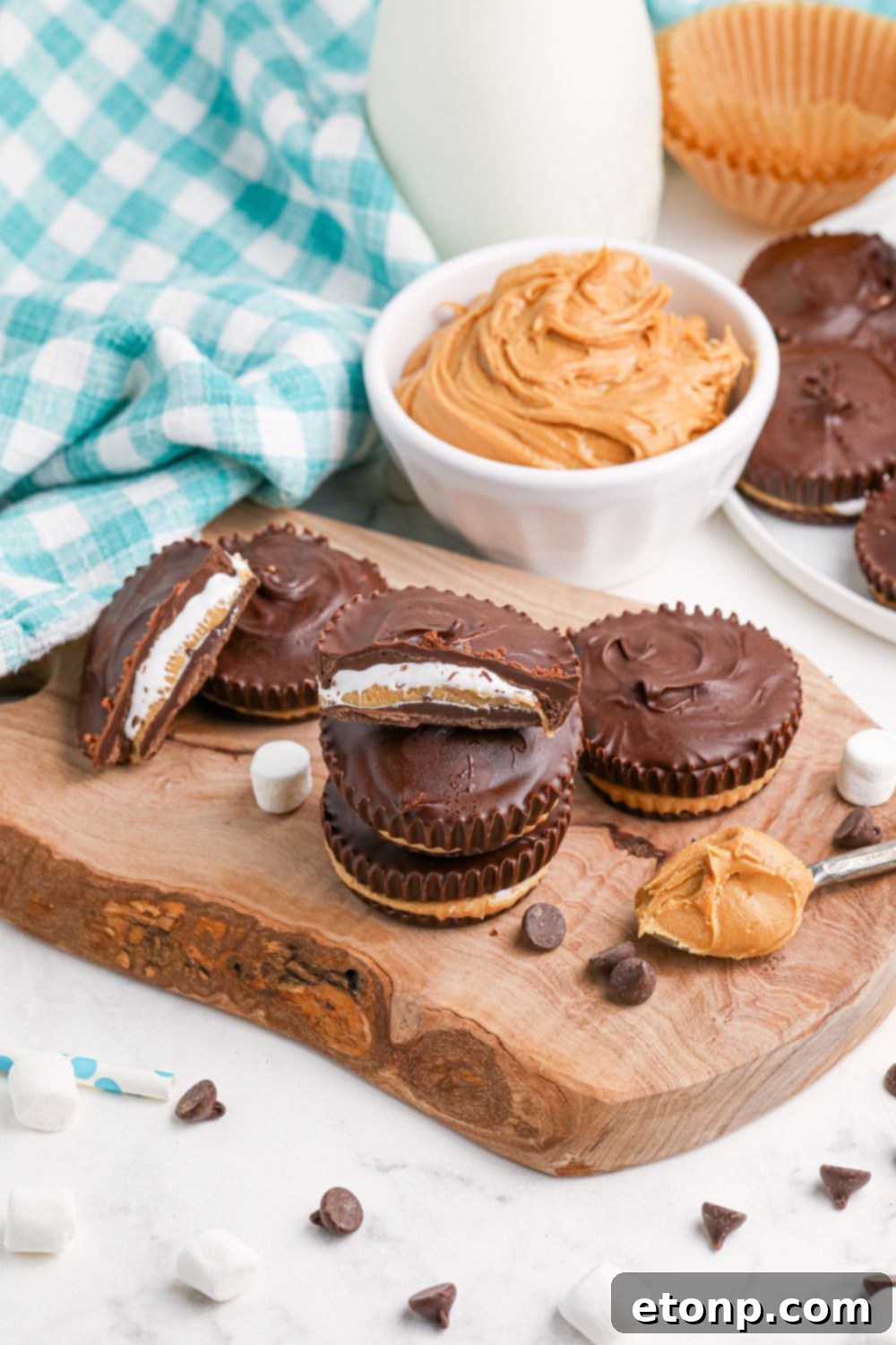 Peanut Butter Marshmallow Cups on table with a bowl of peanut butter behind it and on a spoon next to the cups 