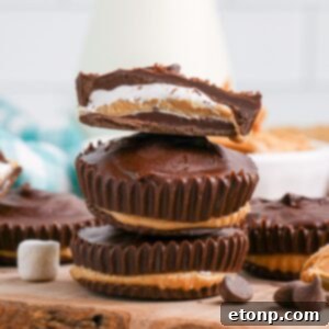 Peanut Butter Marshmallow Cups stacked on wooden cutting board with top one cut in half so you can see the layers