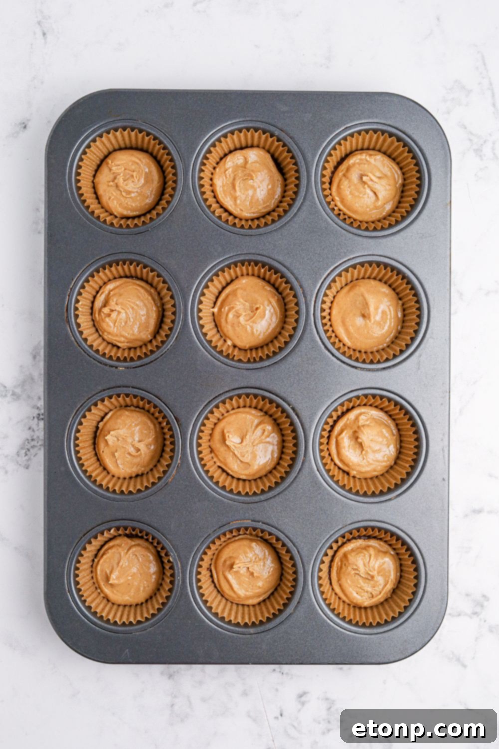 peanut butter poured over chocolate in muffin tin for making Peanut Butter Marshmallow Cups