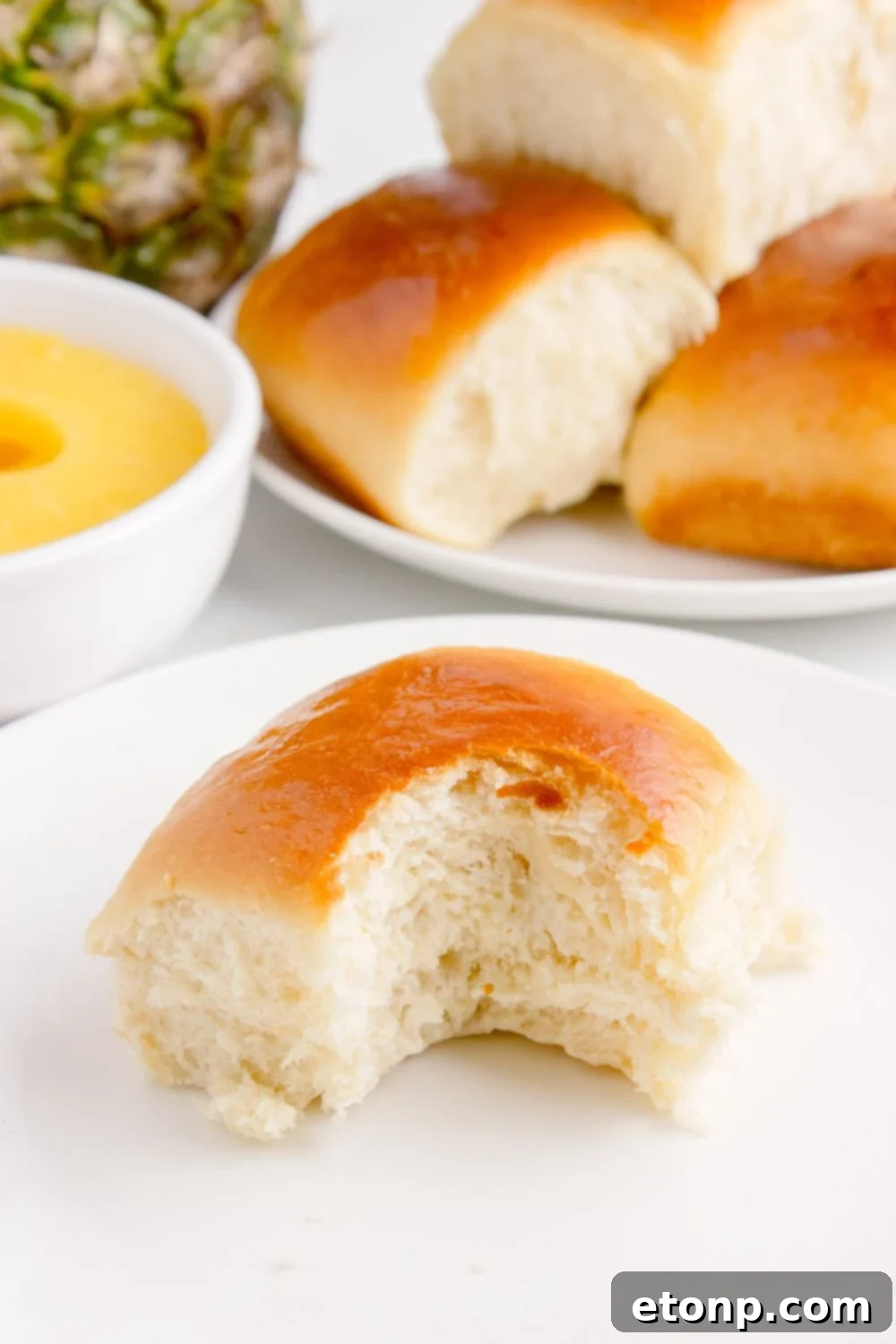 bite taken out of Hawaiian roll on plate with a pan of rolls behind it on table