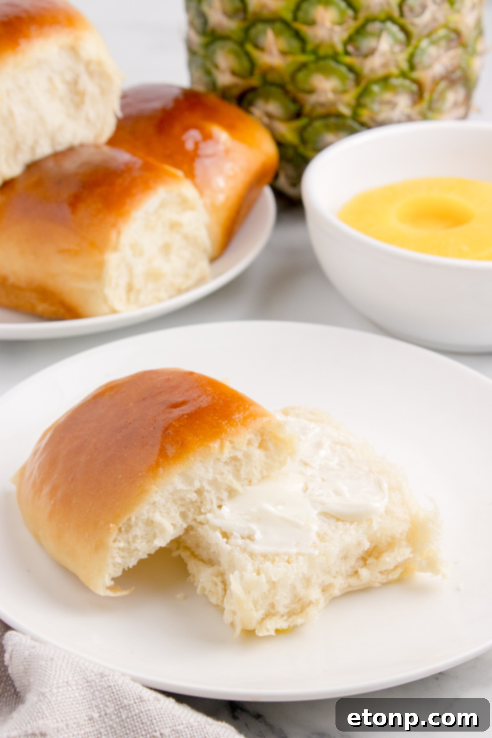 Hawaiian Dinner Roll on plate with it sliced in half and butter spread on it 