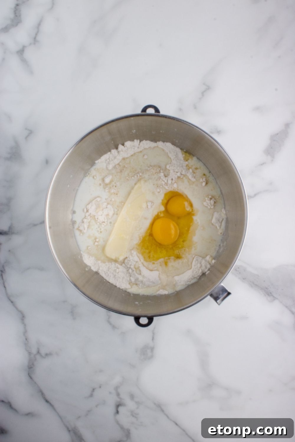 butter and eggs in a flour mixture in a mixing bowl on table for Hawaiian rolls