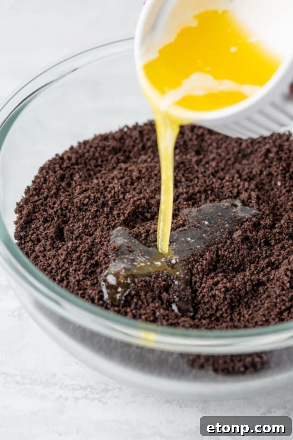 Decadent Chocolate Oreo Dream 6 butter pouring into crushed Oreo cookies in a bowl for the Chocolate Oreo Lush