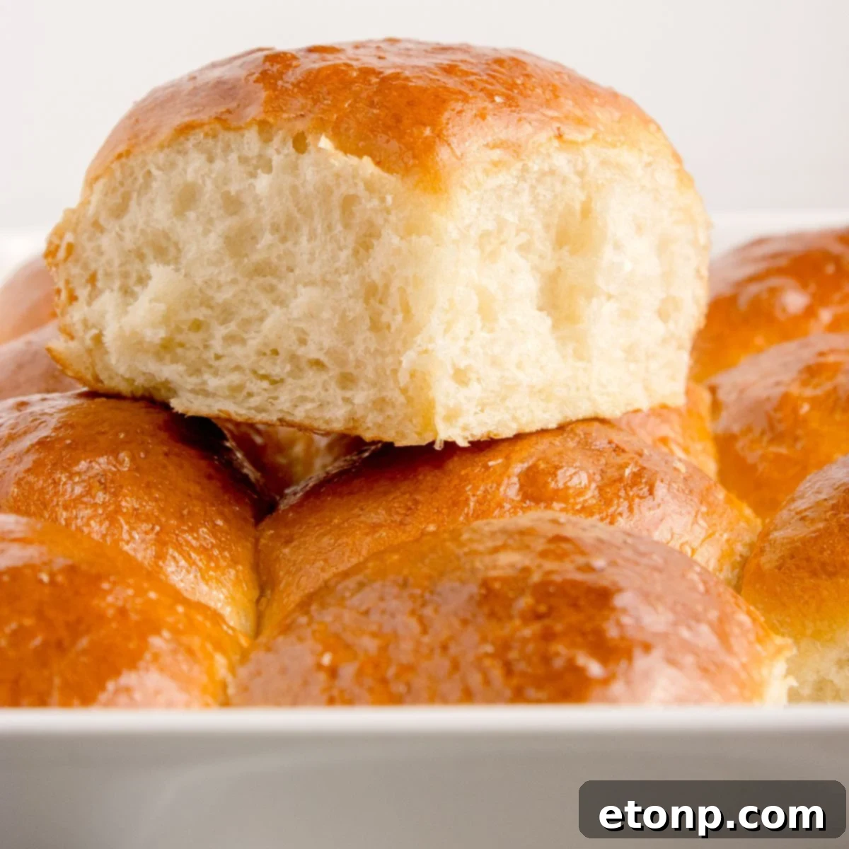 Fluffy golden brown pull apart dinner rolls in a baking pan, with one roll pulled out to show its soft texture