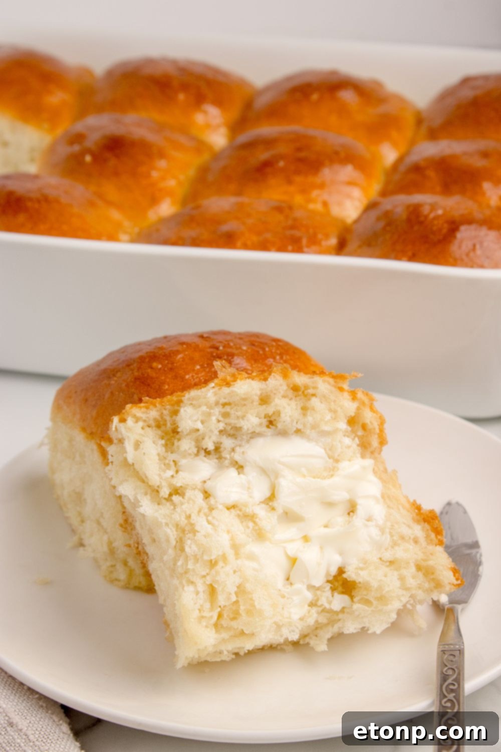 Freshly baked pull apart rolls in a baking pan, with one roll cut in half and generously spread with butter, showcasing its tender interior