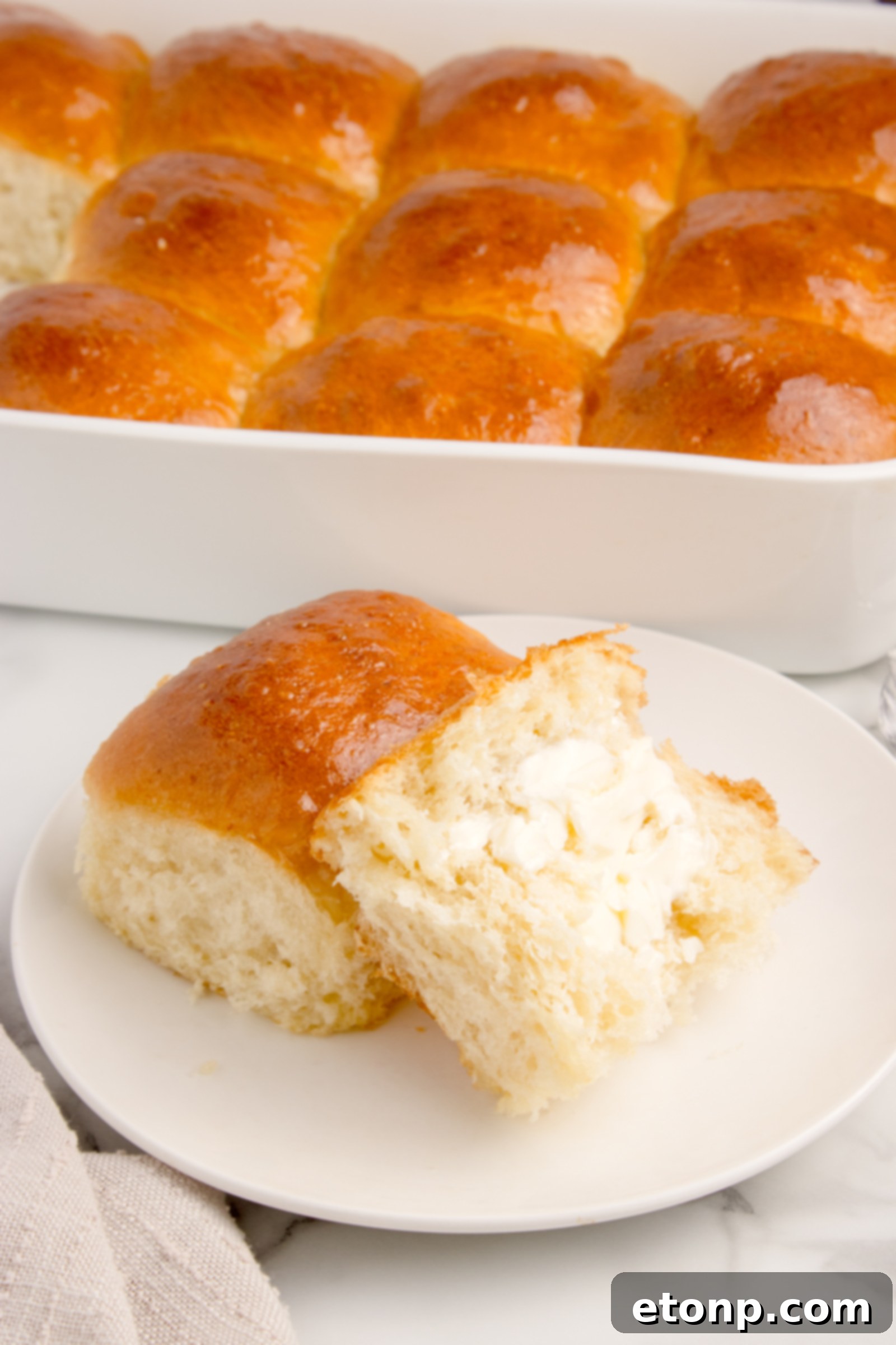 A pull apart dinner roll on a white plate, cut in half and buttered, highlighting its soft interior