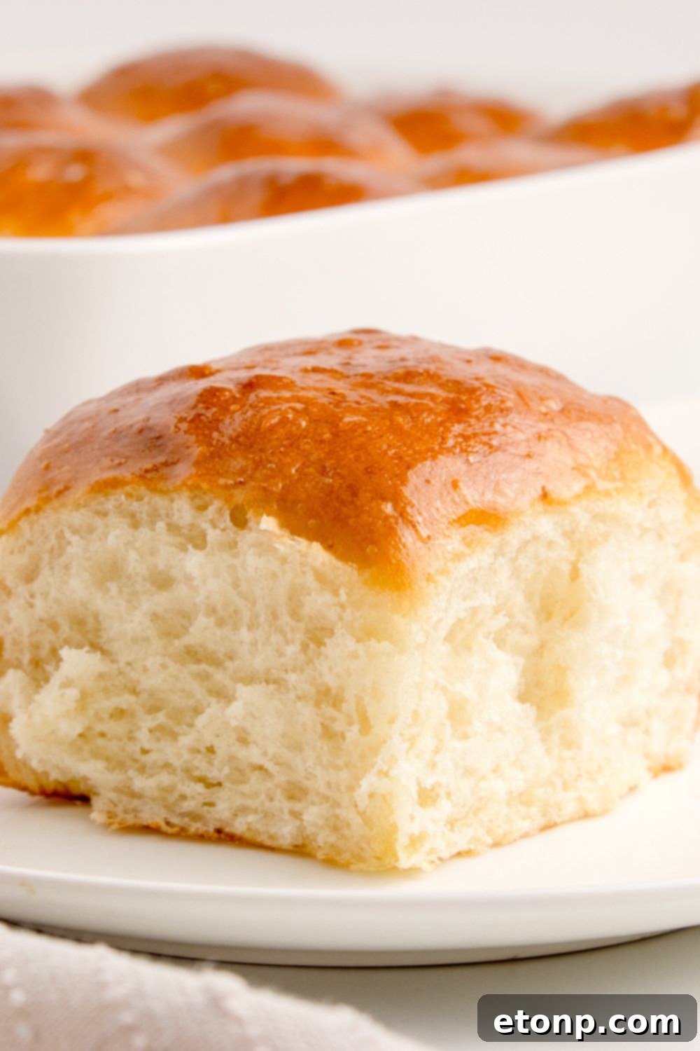A single pull apart roll presented on a plate, with the baking pan full of remaining rolls in the background