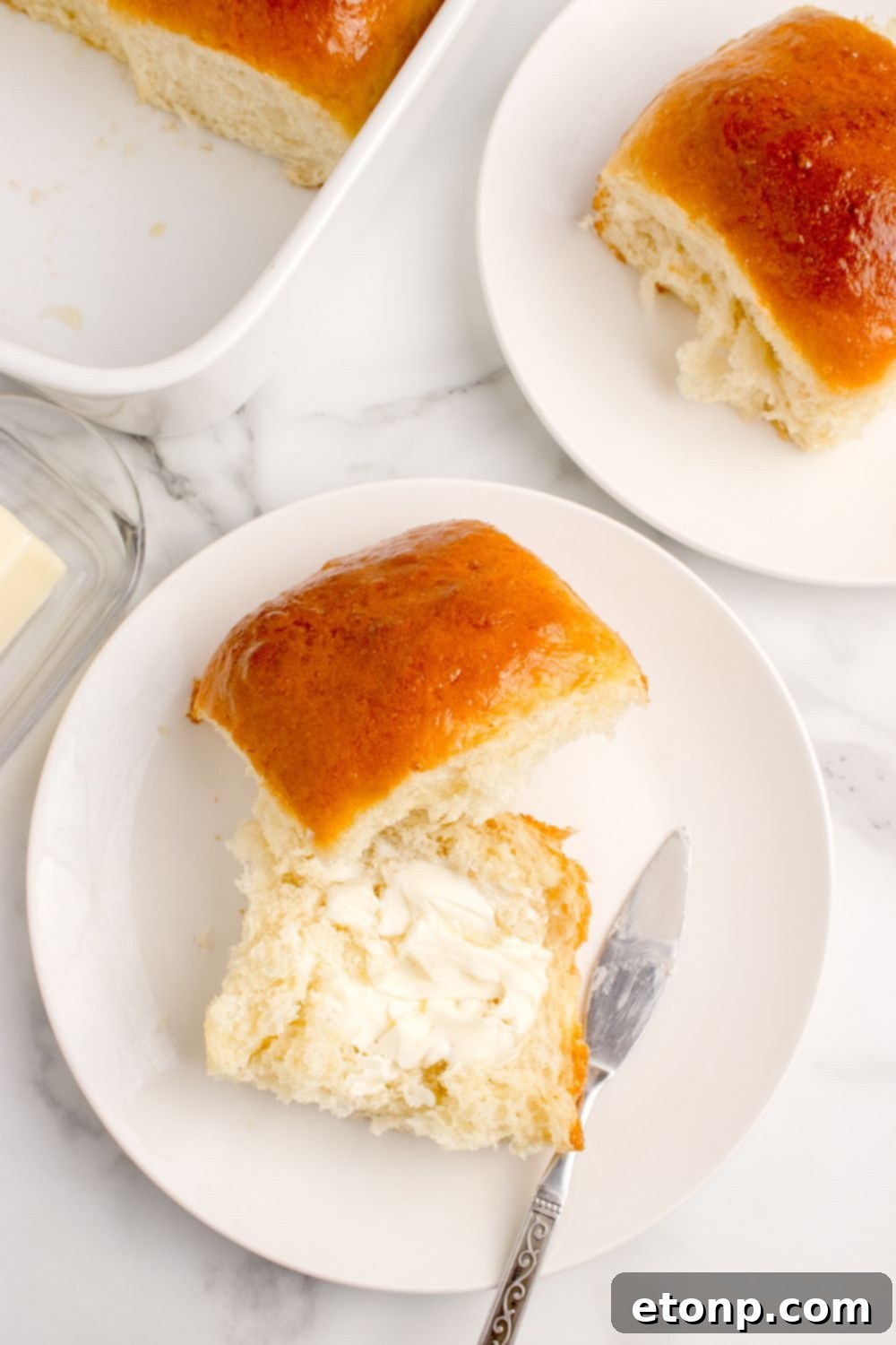 Plates of pull apart dinner rolls, with one roll cut in half and buttered to show its tender interior