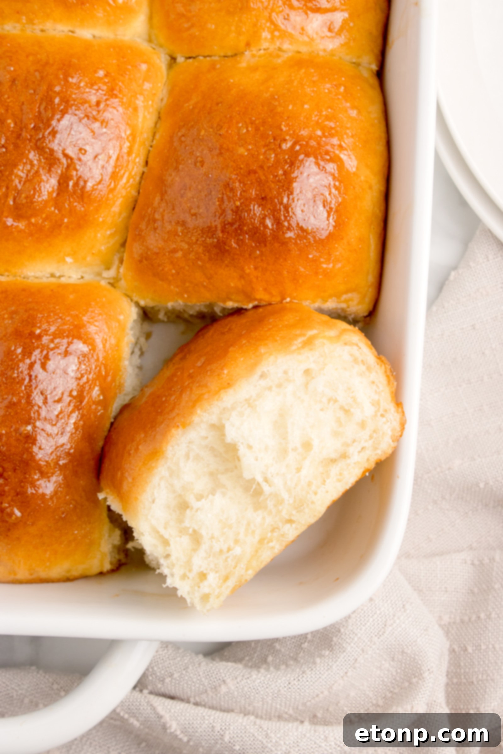 Pull apart dinner rolls in a white baking dish, with one roll removed, showcasing its delicious appeal
