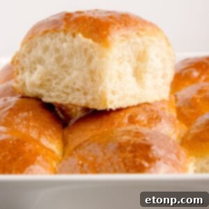 Fluffy golden brown pull apart dinner rolls in a baking pan, with one roll pulled out to show its soft texture