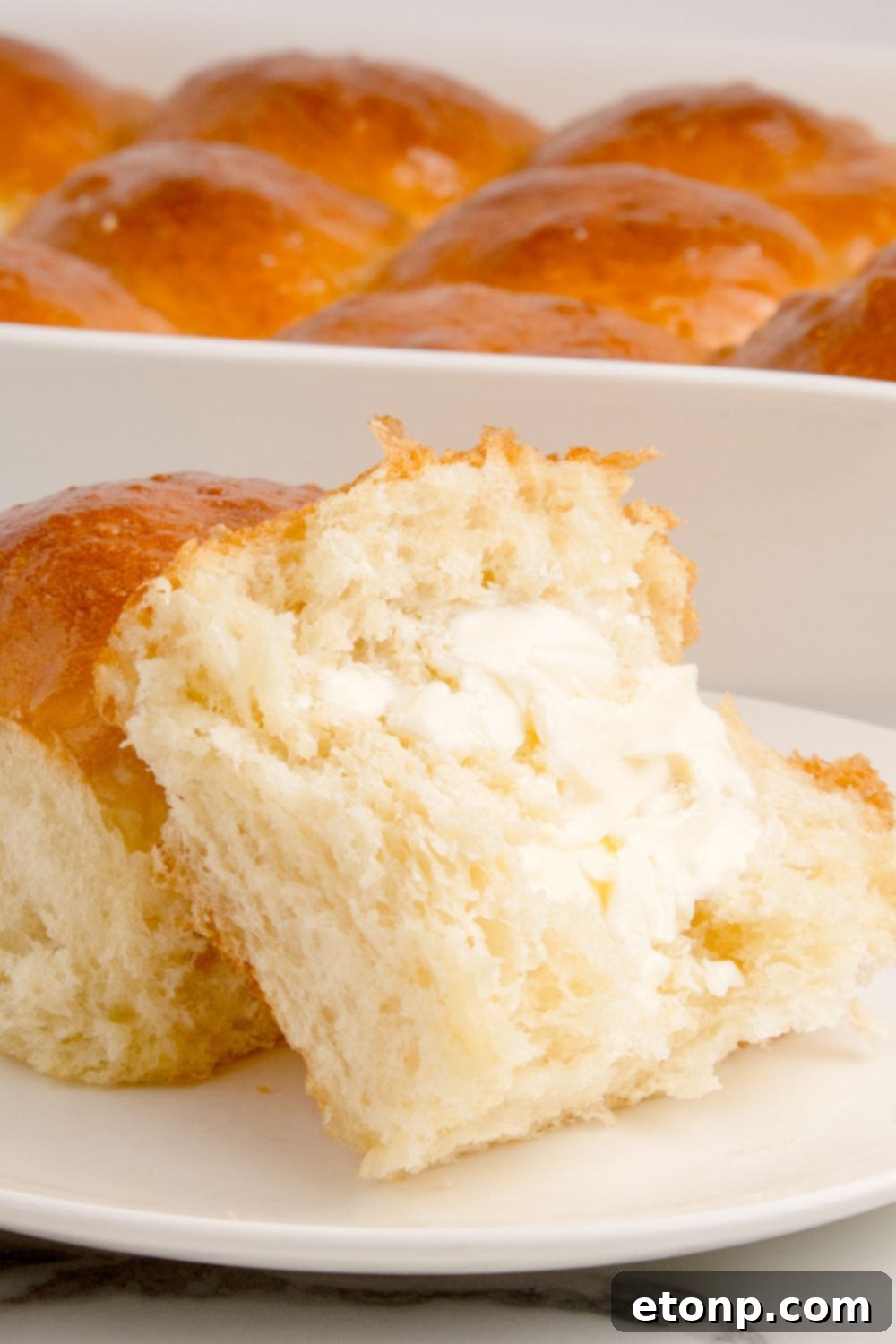 Buttery pull apart dinner rolls in a baking dish, with one roll on a plate, spread generously with butter