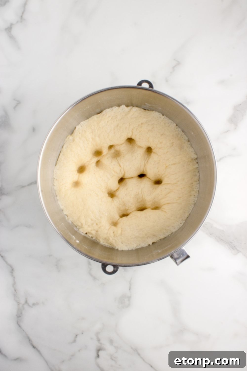 Perfectly risen dough for pull apart rolls in a mixing bowl, gently deflated with fingers