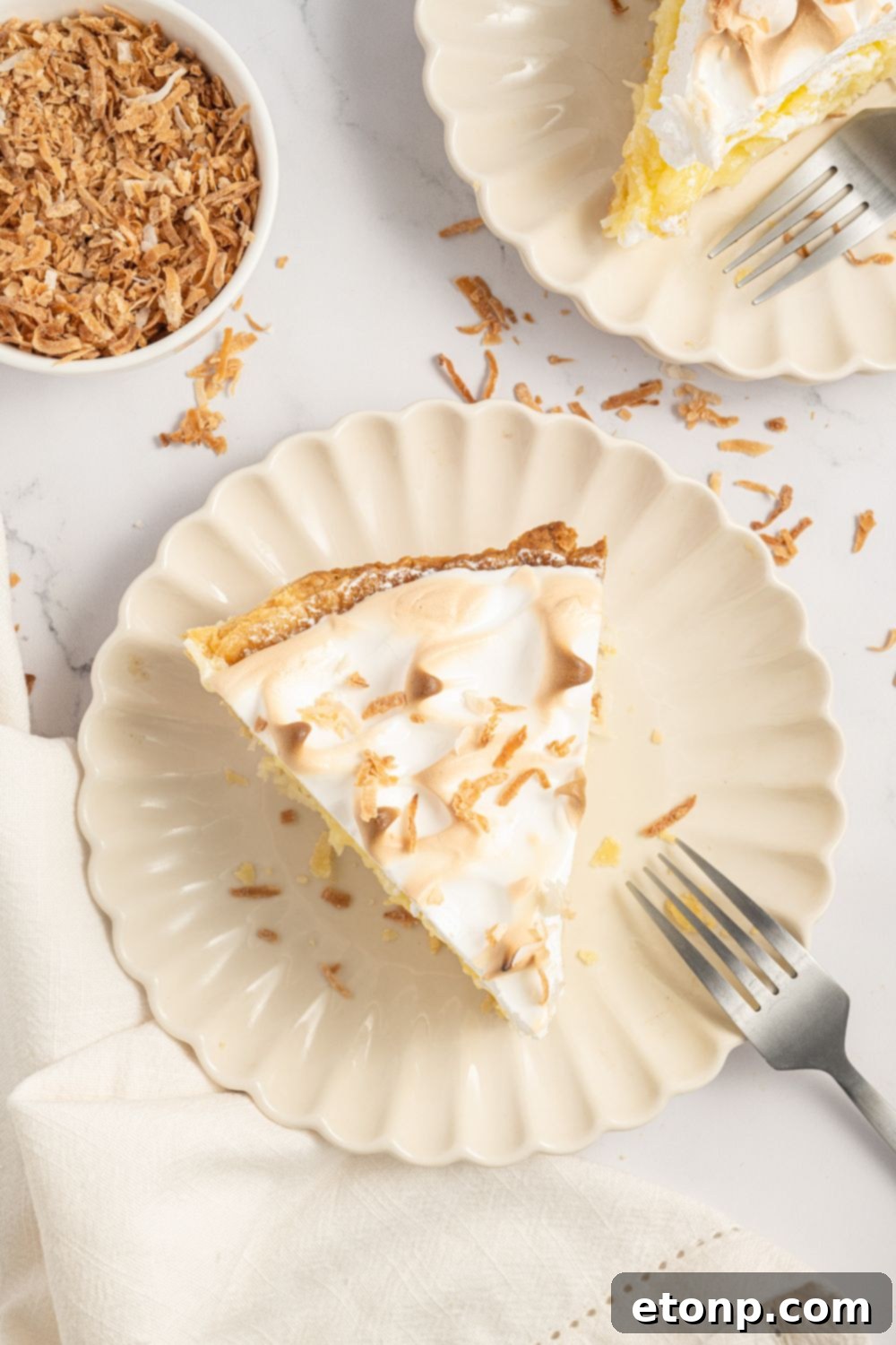 slices of Coconut Meringue Pie on plates with forks and toasted coconut flakes around the plate