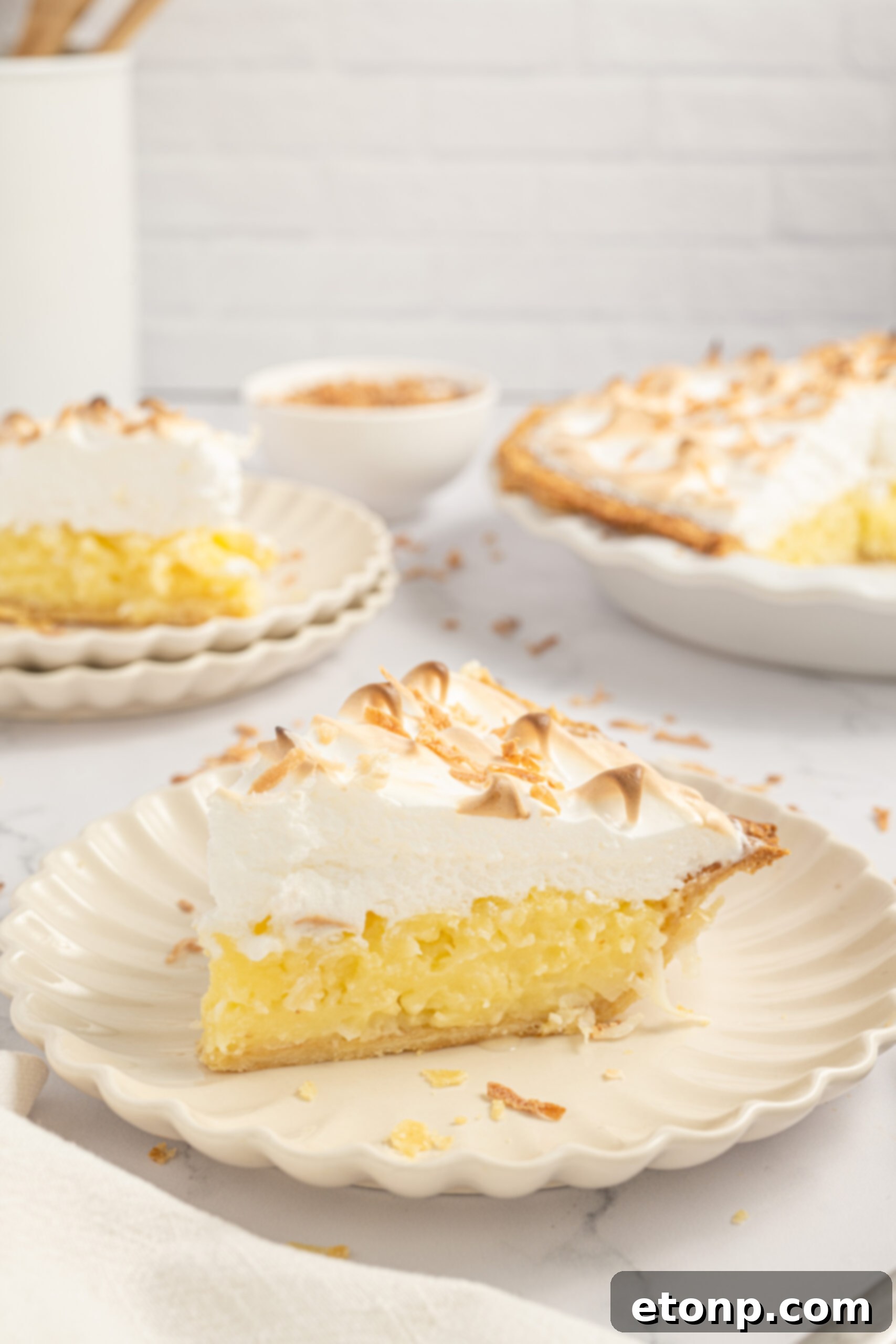 Coconut Meringue Pie on plate with toasted coconut sprinkled around it on table