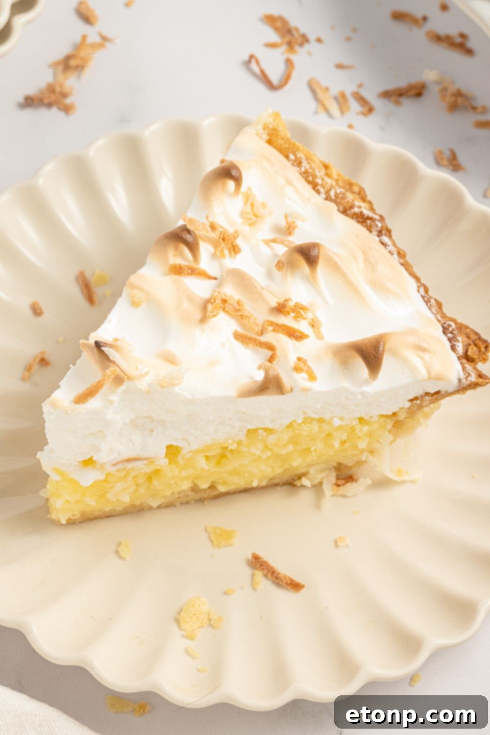 Coconut Meringue Pie on plate with toasted coconut sprinkled around it on table