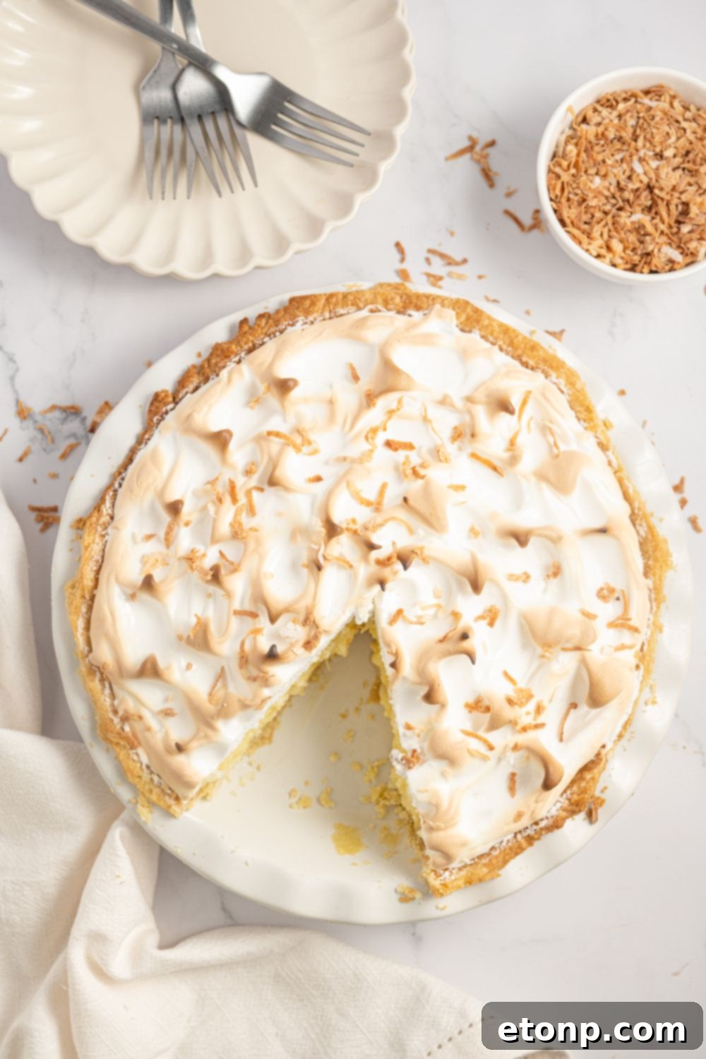 overhead of Coconut Meringue Pie on table with a small plate to the side and toasted coconut flakes