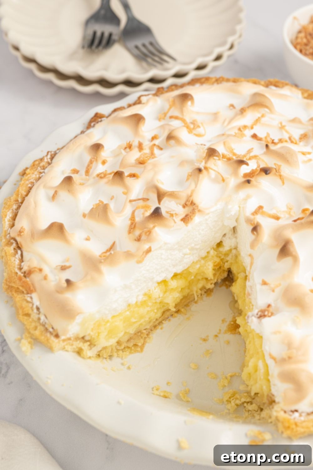Coconut Meringue Pie in a pie plate with one slice taken out so you can see the filling and meringue layers