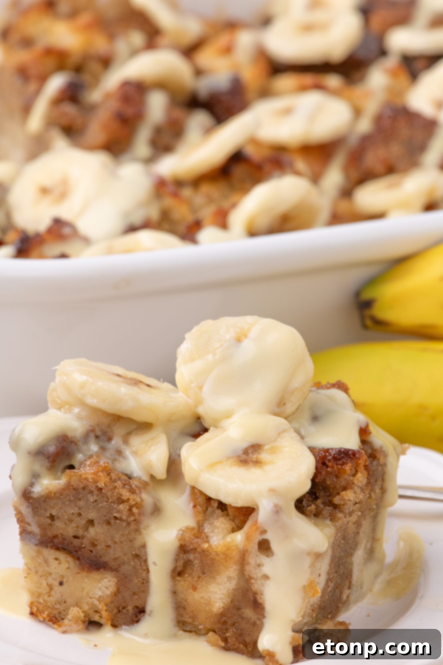 a white plate with a slice of Banana Bread Pudding on it topped with sliced bananas 
