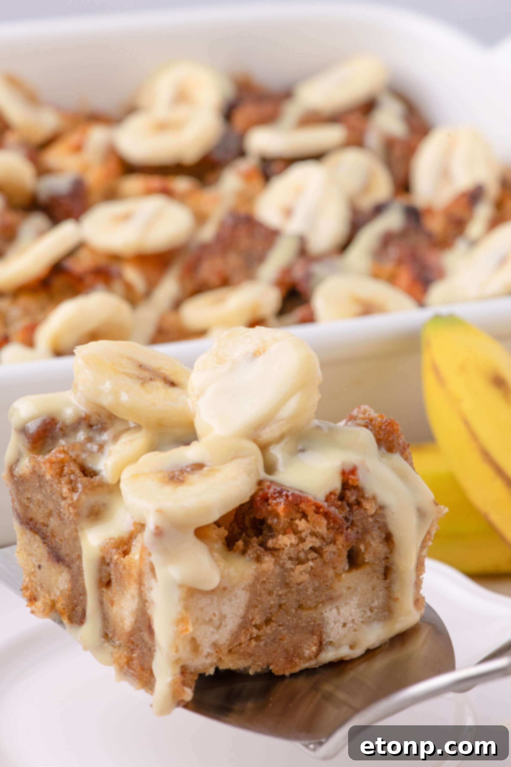 a silver spatula with a slice of Banana Bread Pudding on it topped with sliced bananas 