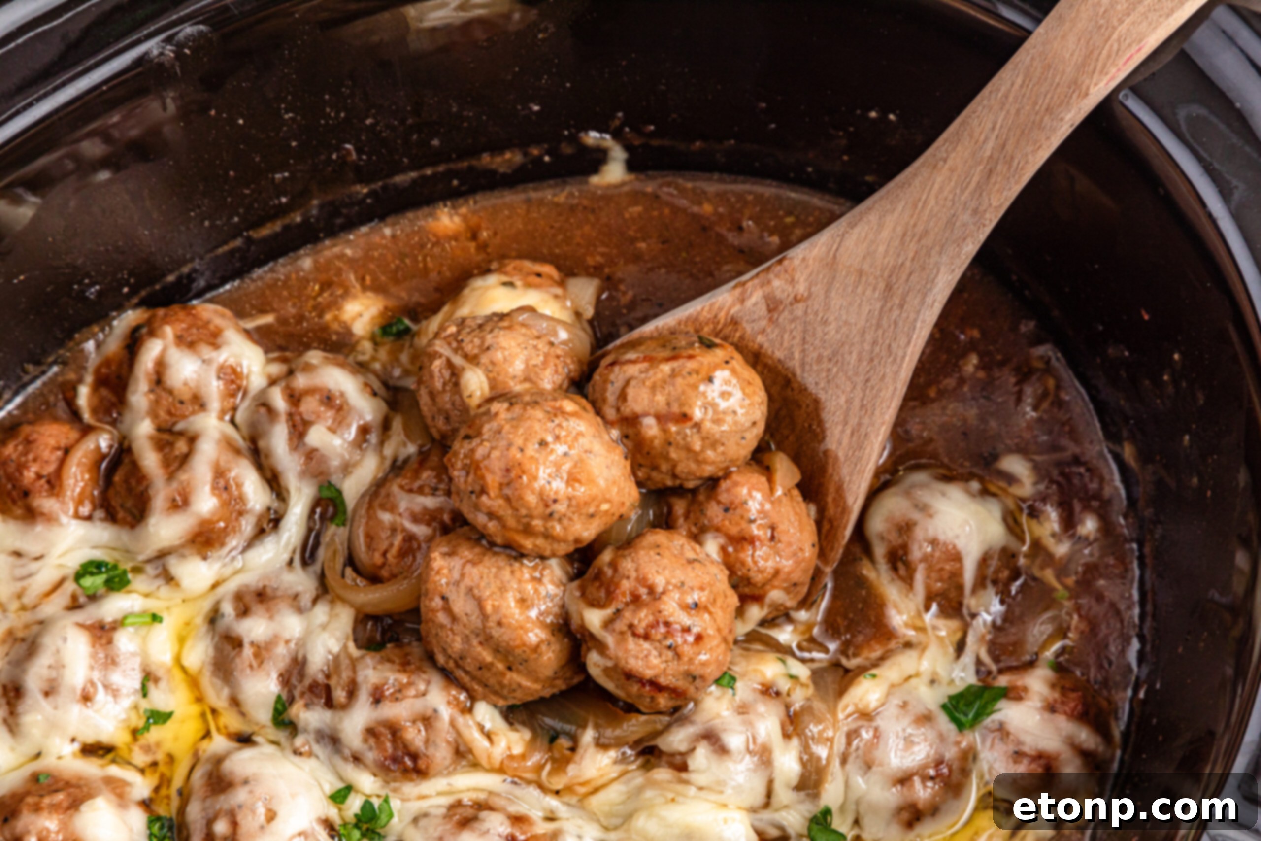 Crock Pot French Onion Meatballs with some being scooped out of slow cooker with spoon 