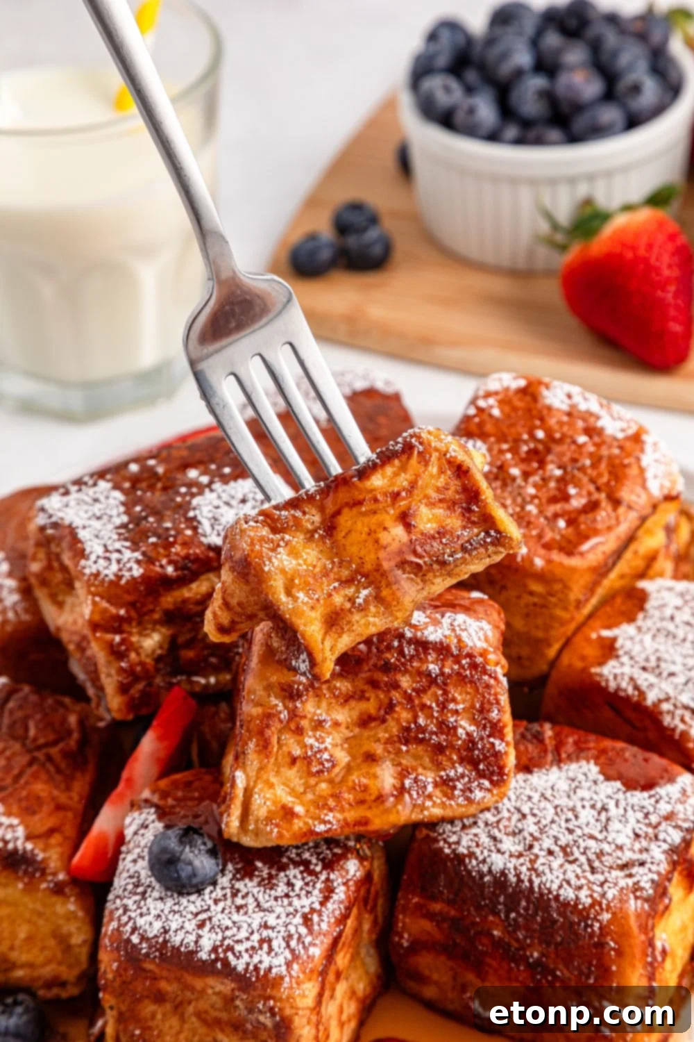 a fork piercing a piece of Hawaiian Roll French Toast on a plate, highlighting its soft texture