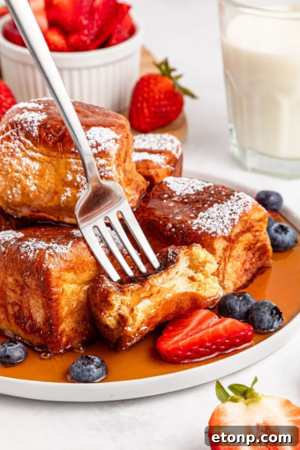 a fork gently poking into a piece of Hawaiian Roll French Toast on a white plate