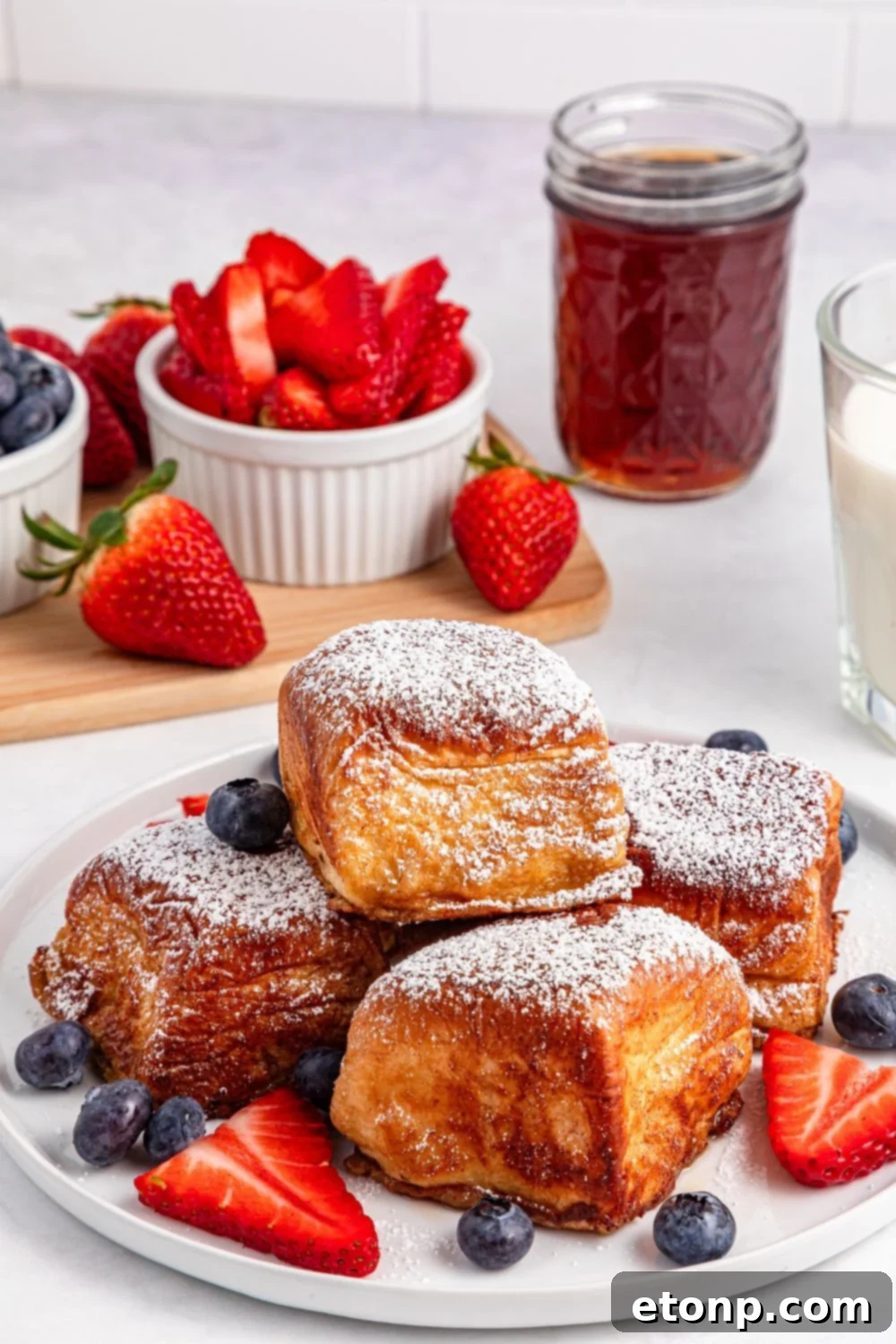 Hawaiian Roll French Toast stacked high on a plate, surrounded by fresh berries and a bowl of strawberries
