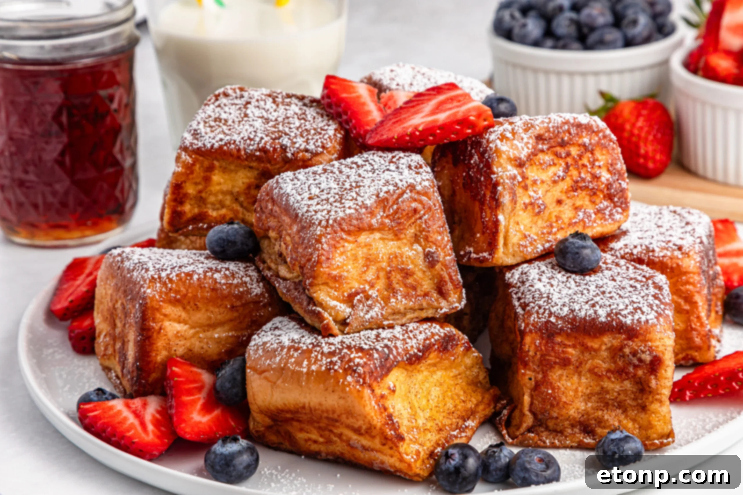 a white plate full of Hawaiian Roll French Toast, elegantly topped with sliced strawberries and blueberries