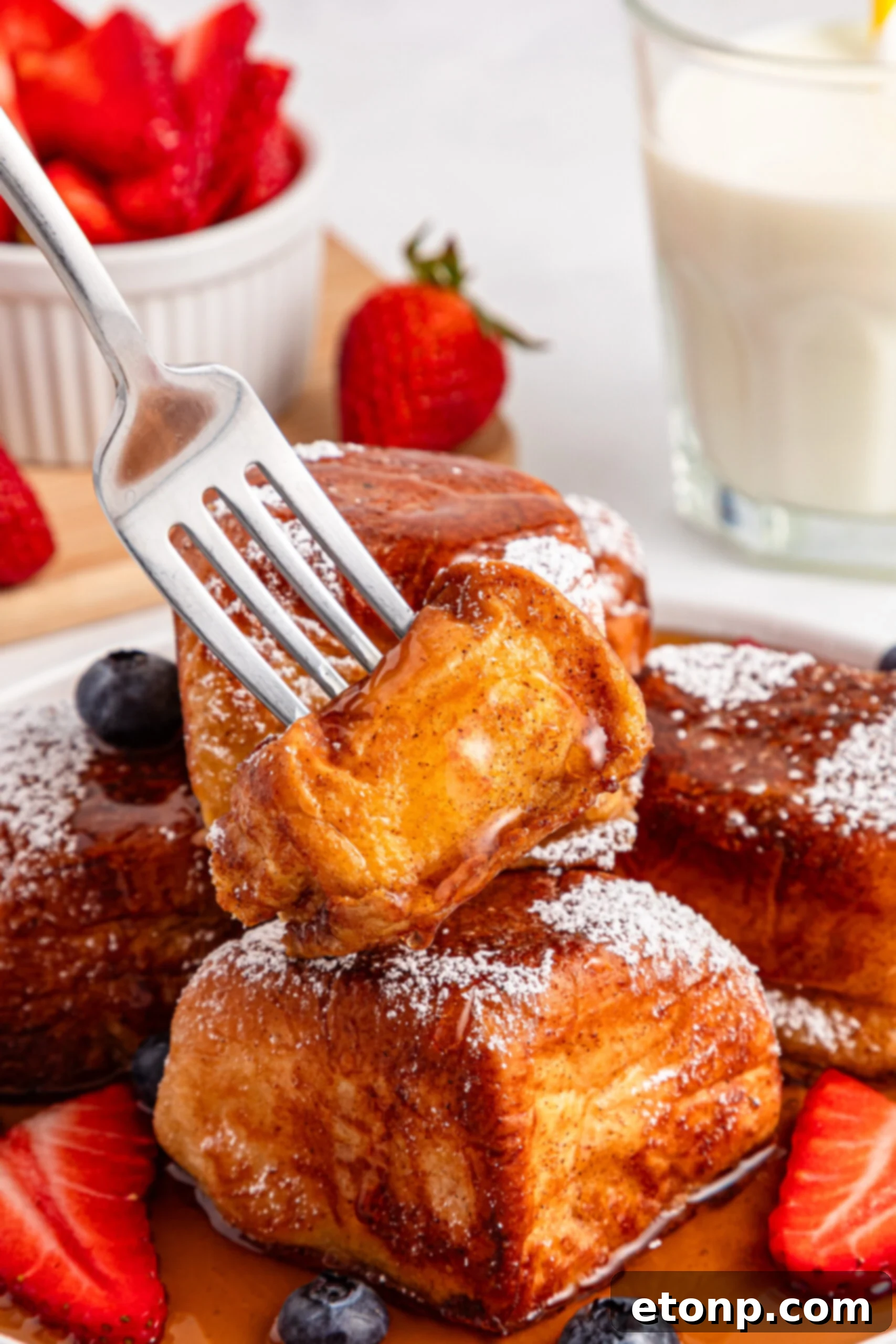 syrup being drizzled on a fork-lifted piece of Hawaiian Roll French Toast, emphasizing its deliciousness