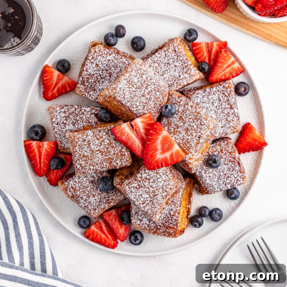 perfectly stacked Hawaiian Roll French Toast on a plate, adorned with powdered sugar and fresh fruit