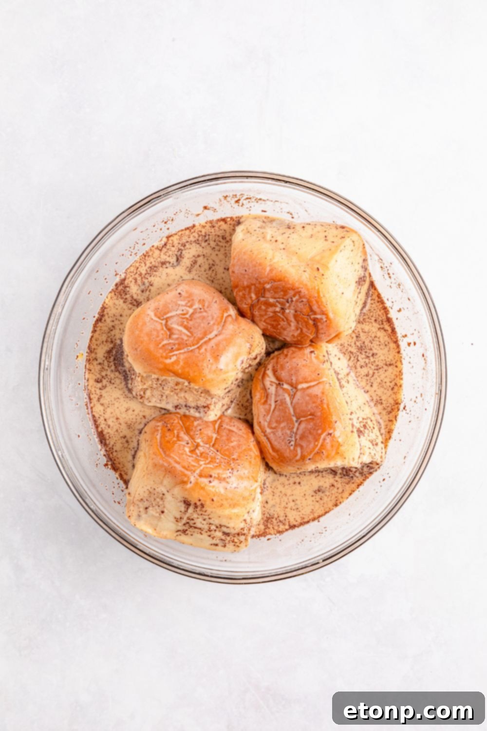 Hawaiian sweet rolls gently soaking in the French toast mixture in a glass bowl on a kitchen table