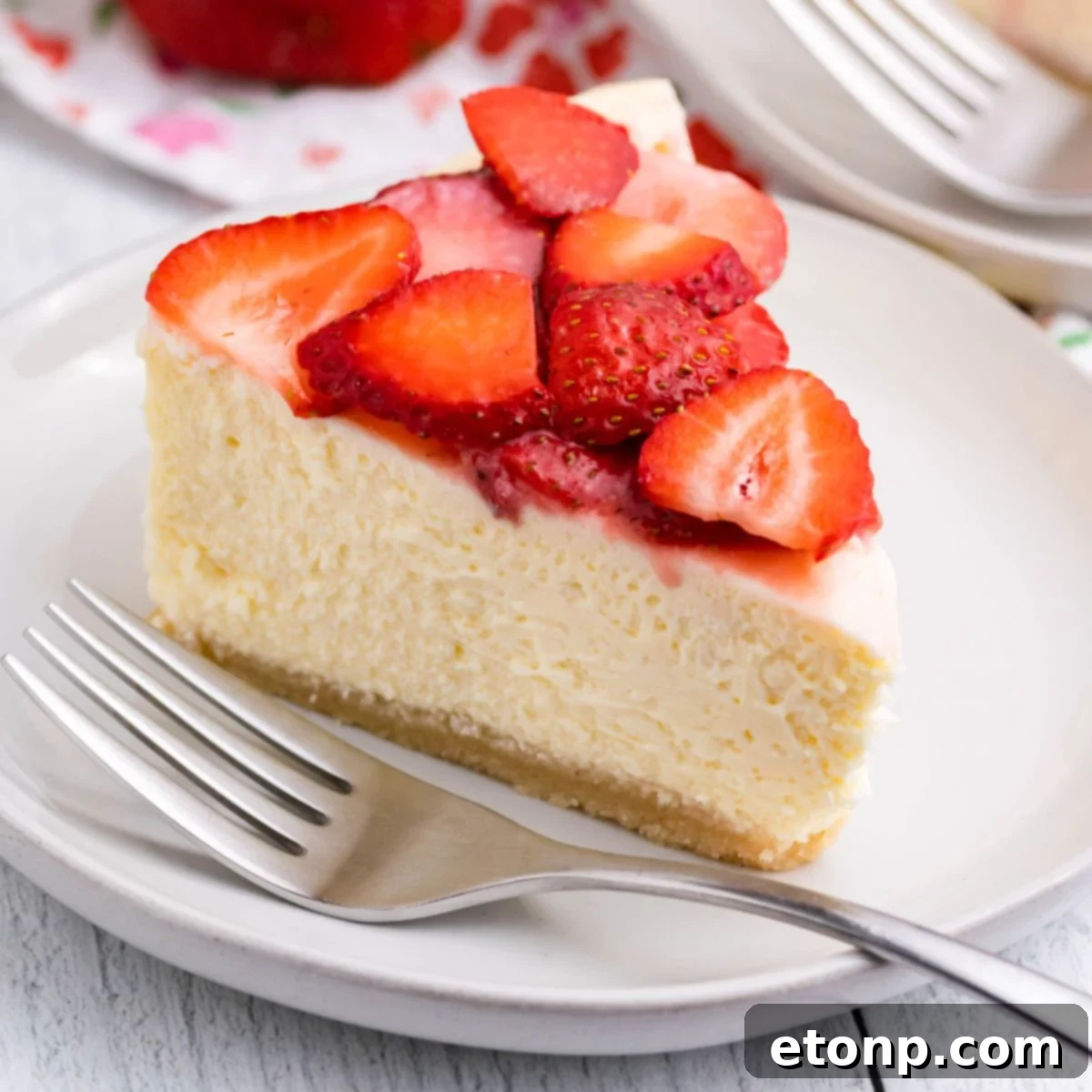 slice of keto cheesecake on a plate topped with strawberries and fork on the side of plate 