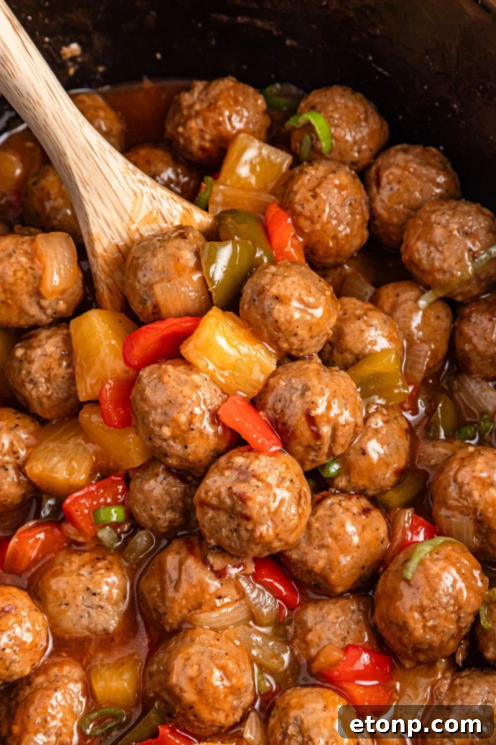 meatballs in slow cooker with a wooden spoon scooping out