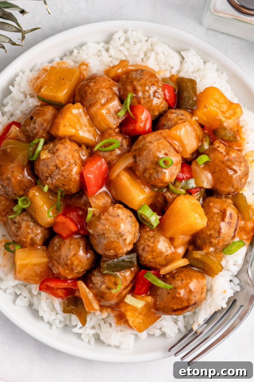 Sweet And Sour Meatballs over a bed of rice on plate on table 