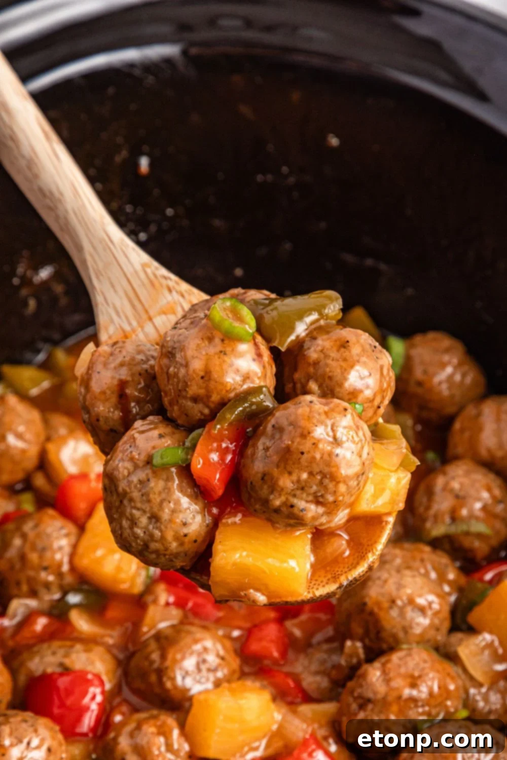 wooden spoon above crock pot with sweet and sour meatballs on spoon
