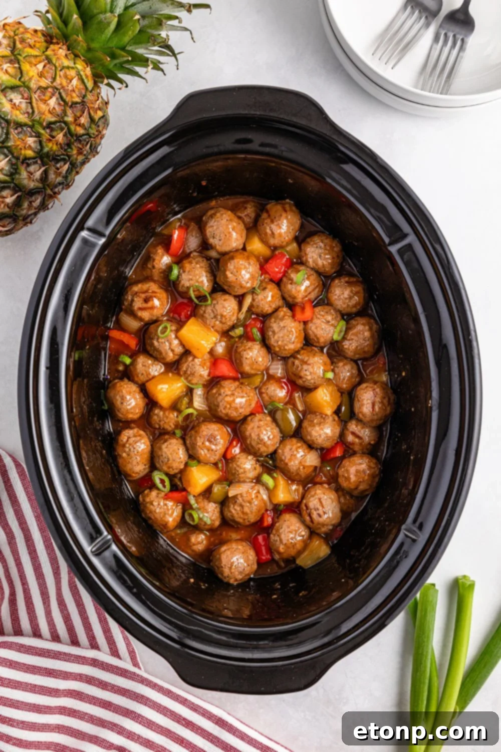 Crock Pot Sweet And Sour Meatballs in a crock pot sitting on table with pineapple and green onions on side of table 