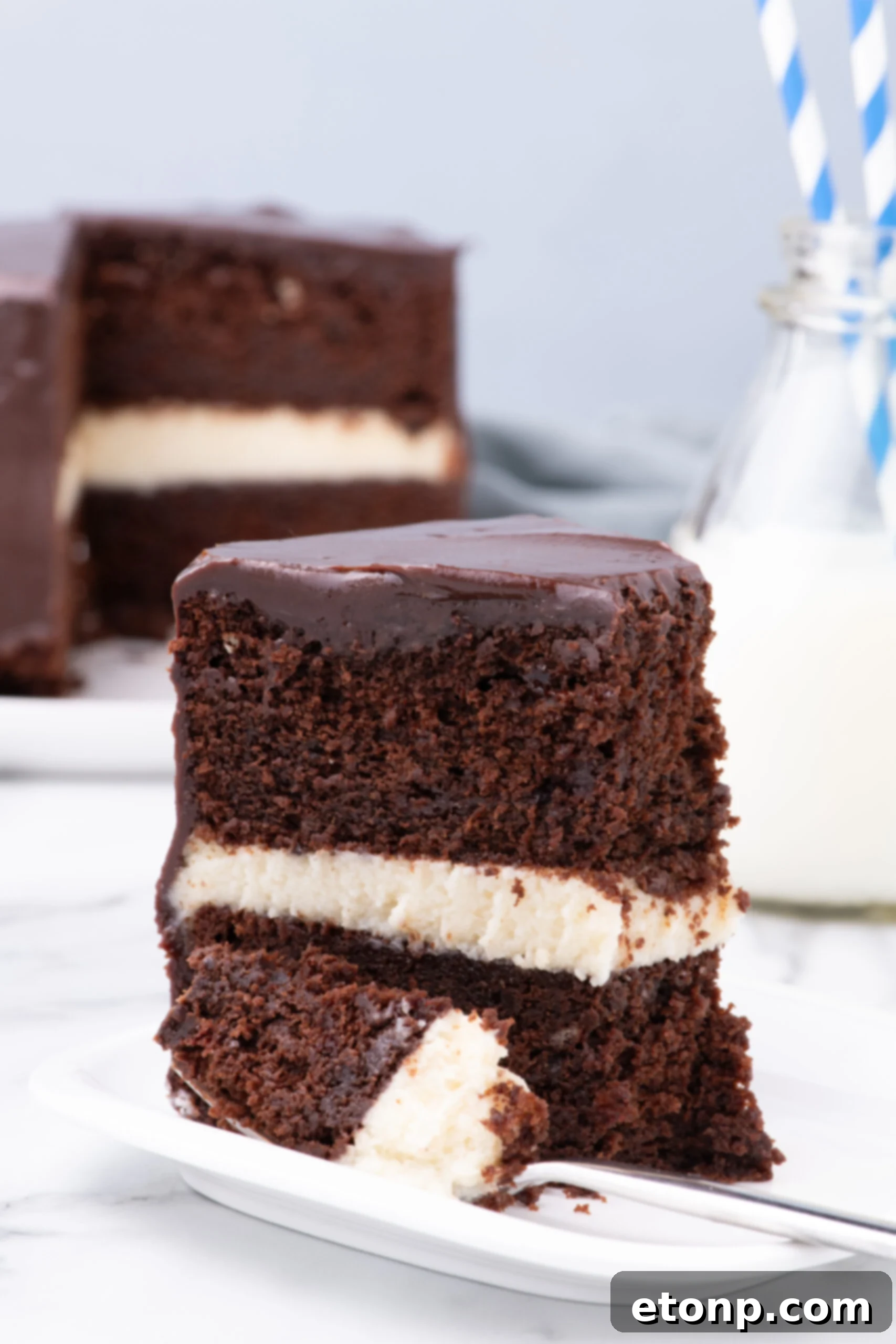 Slice of Ding Dong Cake on a white plate with the whole cake in the background 