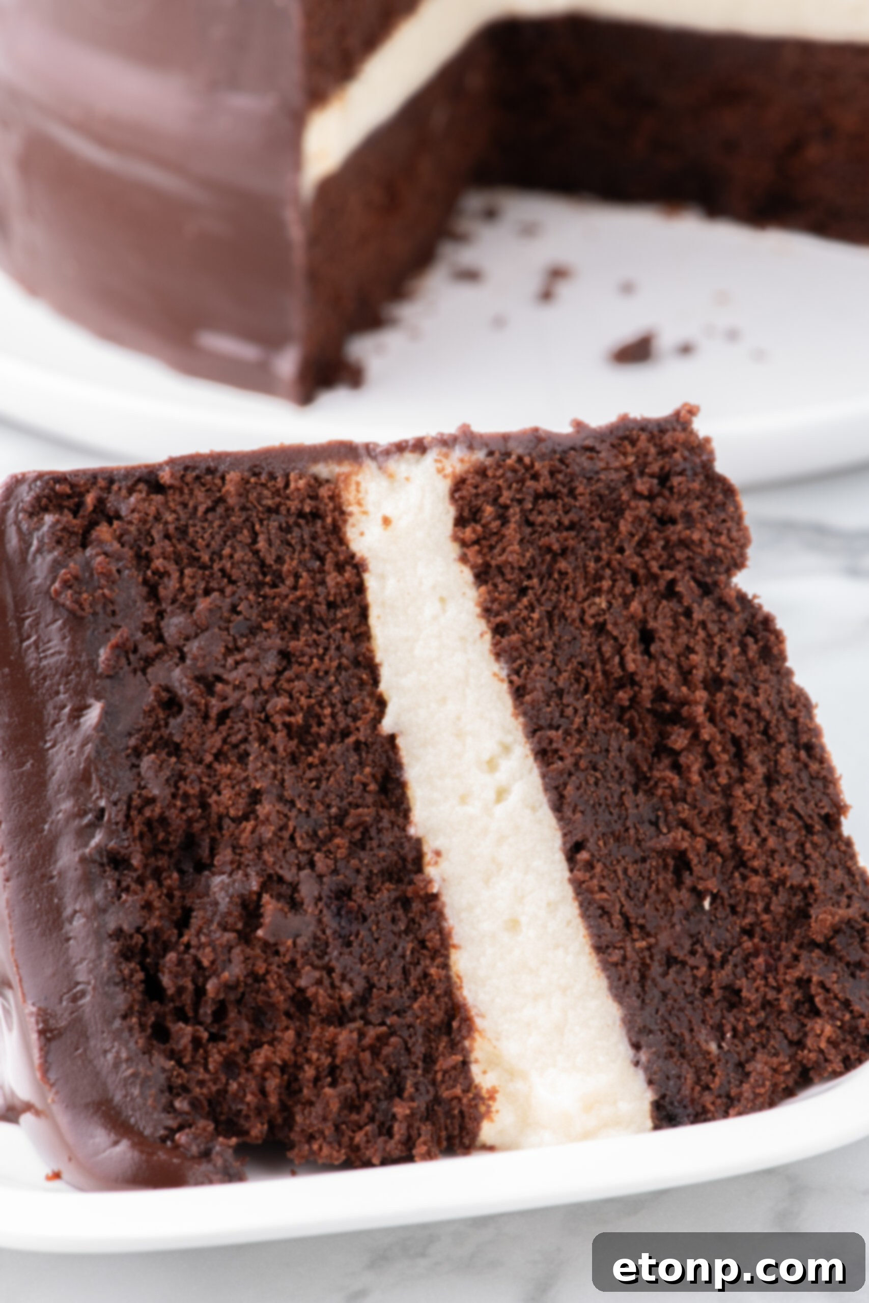 Very close up angle of a Slice of Ding Dong Cake on a white plate with the whole cake in the background 