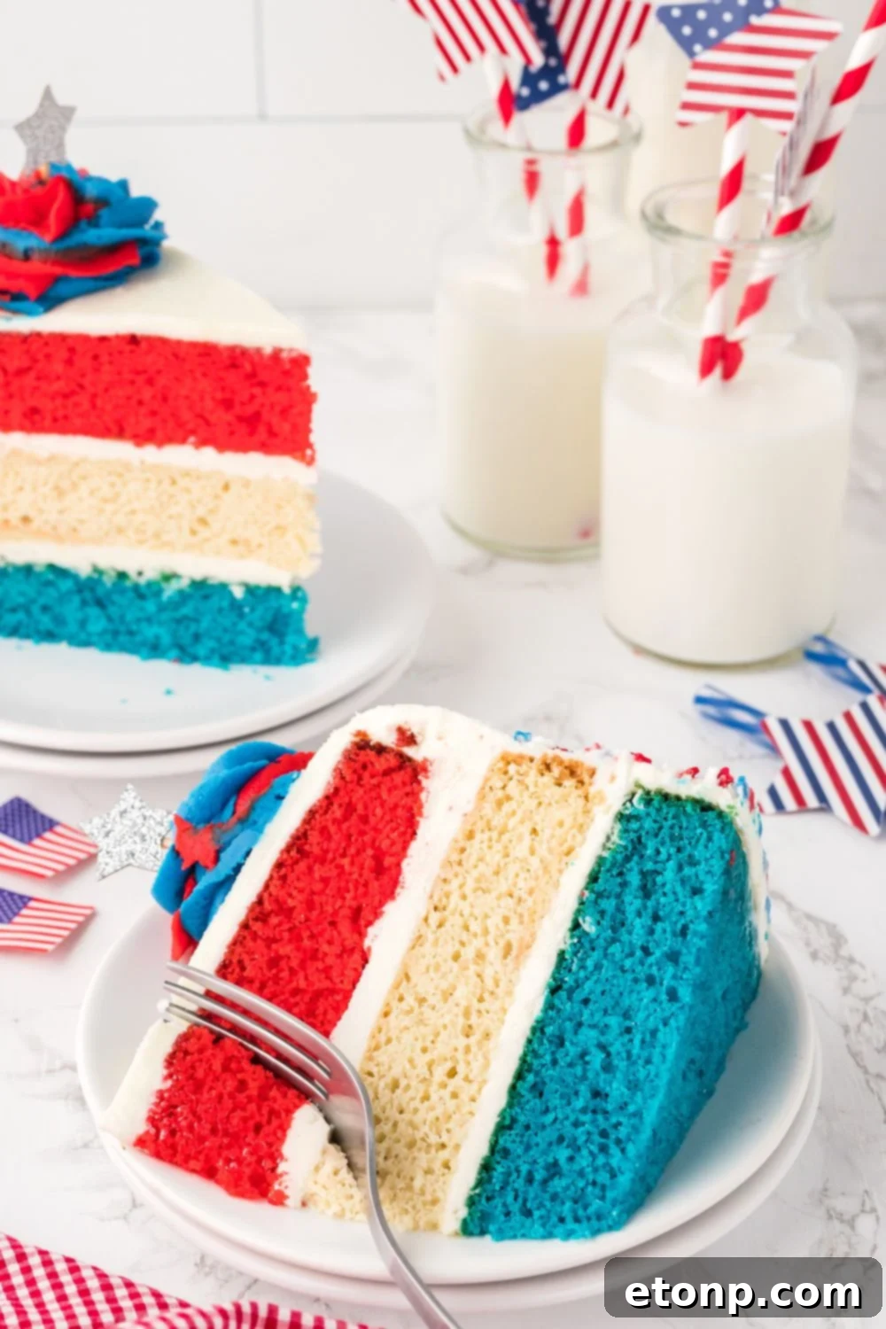 slice of american flag cake on plate with a fork poking in it, and glasses of milk behind it on table