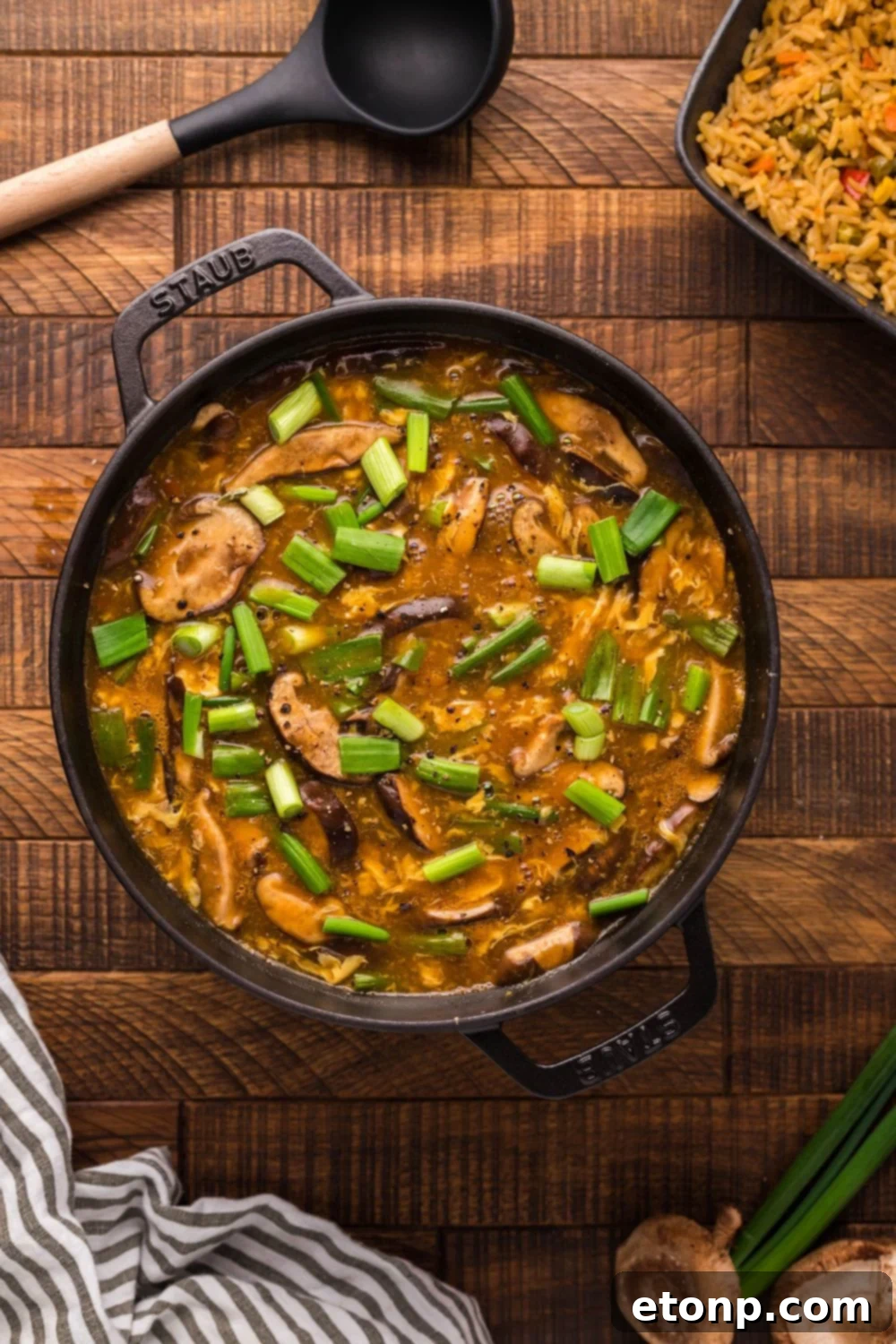 A large pot of freshly made P.F. Chang's Hot and Sour Soup on a wooden table, accompanied by a serving spoon and a towel