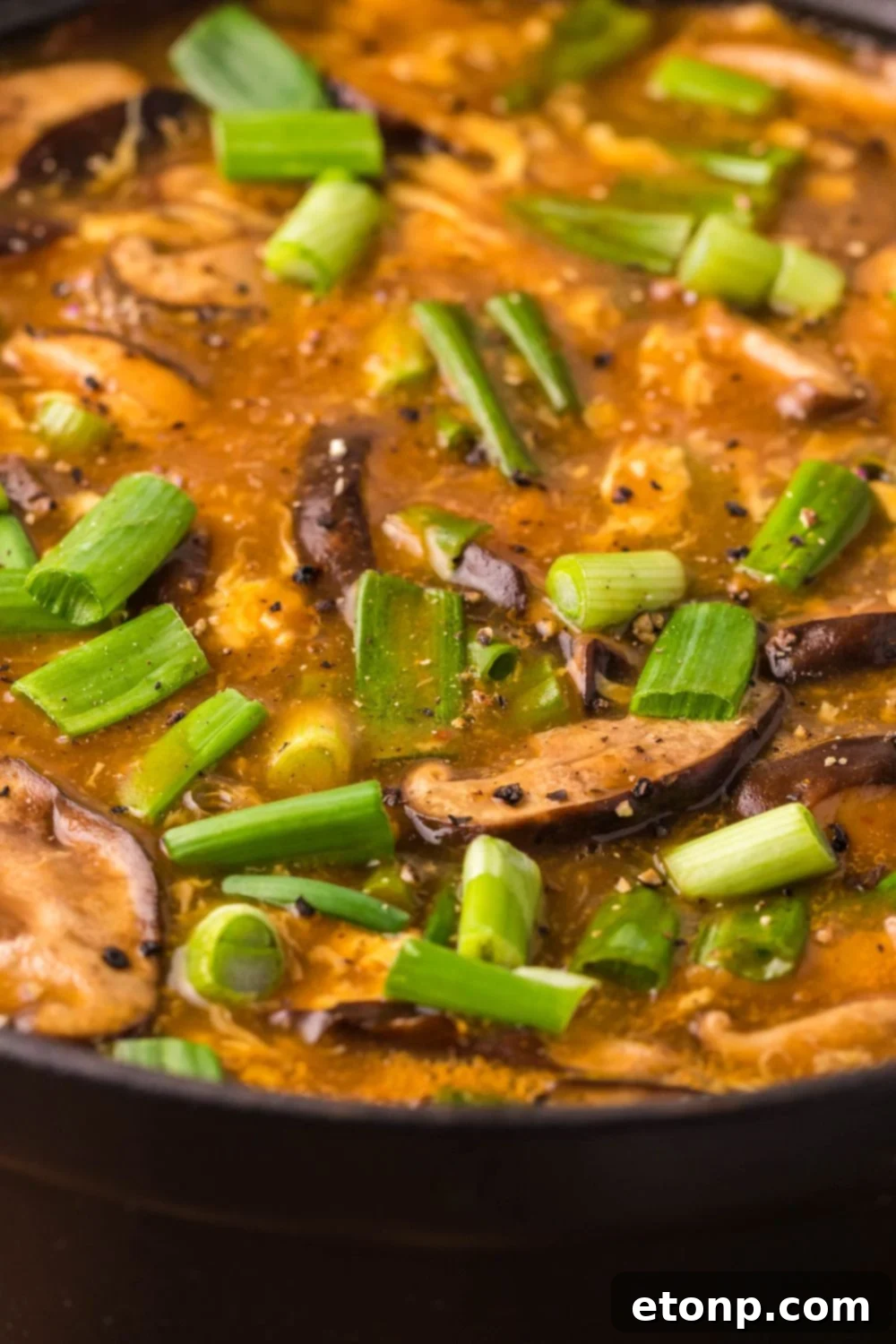 A close-up view of P.F. Chang's Hot and Sour Soup simmering in a metal pan on a wooden table, steam rising