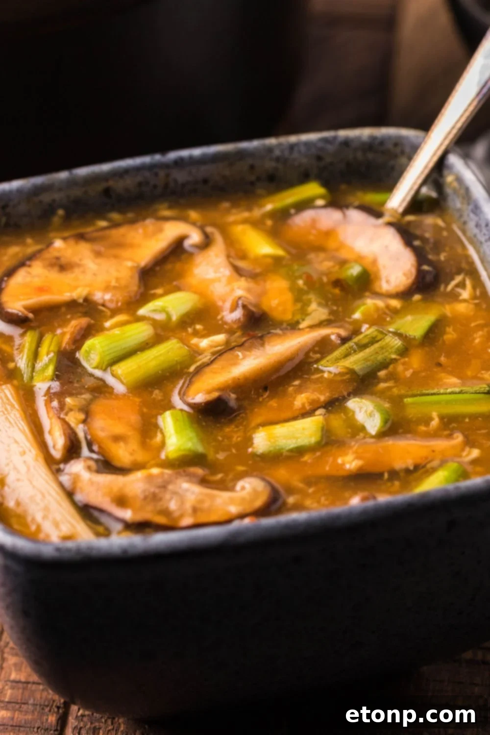 P.F. Chang's Hot and Sour Soup served in a square bowl with a spoon, on a wooden table