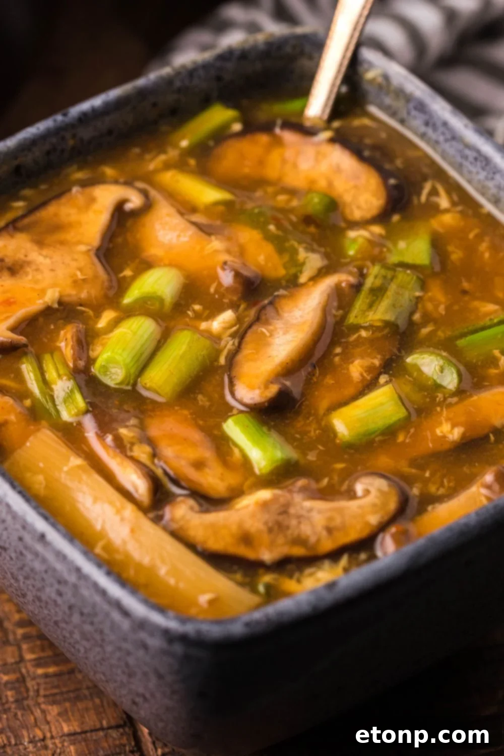 A square bowl filled with P.F. Chang's Hot and Sour Soup, featuring visible mushrooms and tofu, with a spoon resting in the bowl