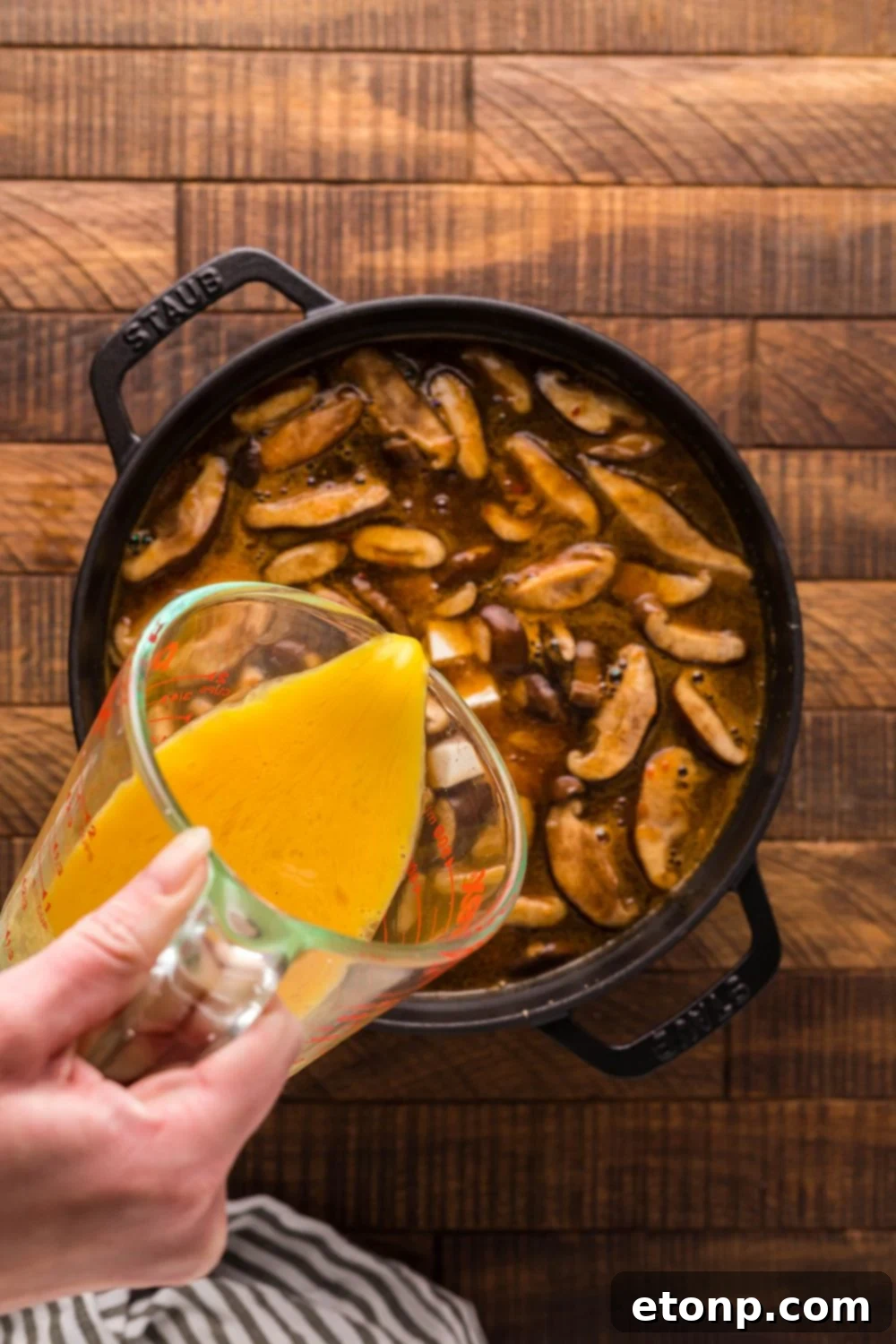Beaten eggs being slowly poured into hot P.F. Chang's Hot and Sour Soup in a pot, creating delicate ribbons