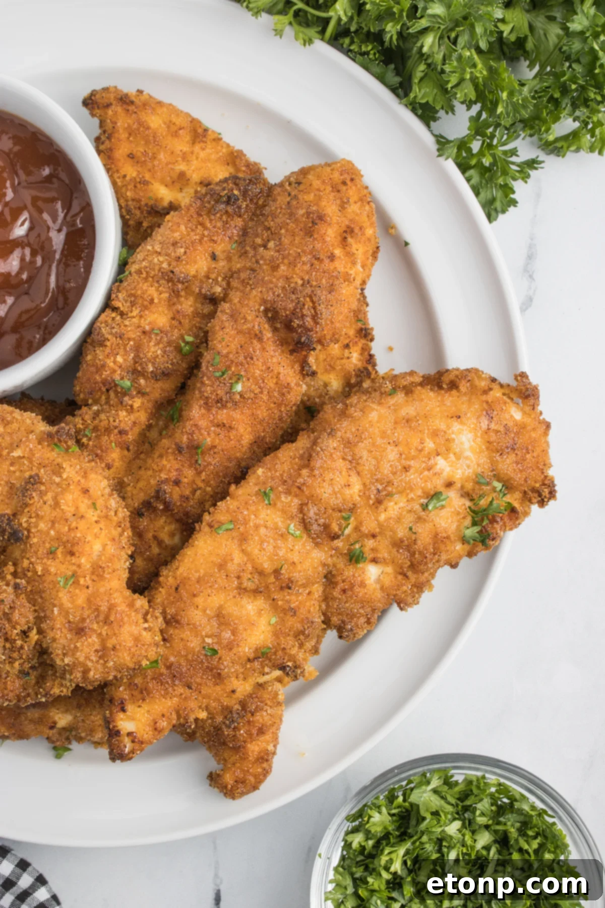 Air Fryer Chicken Tenders on a white plate with a small cup of BBQ sauce on the side 