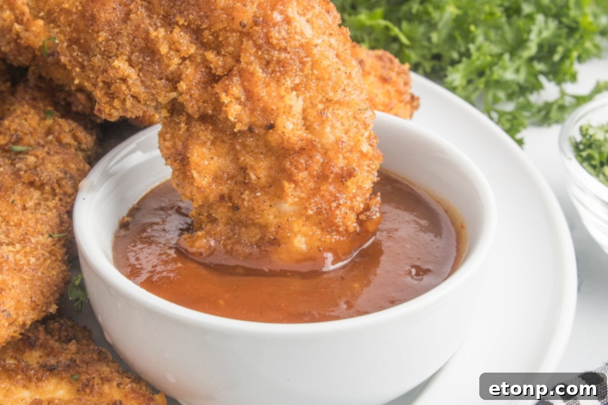 up close shot of Air Fryer Chicken Tender being dipped into BBQ sauce  