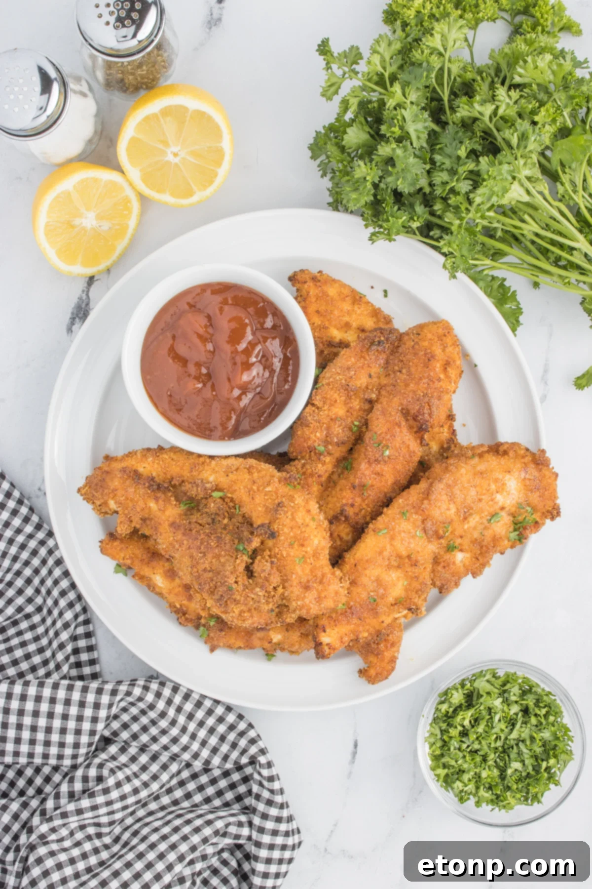 overhead view of Air Fryer Chicken Tenders on a white plate with a small cup of BBQ sauce on the side 